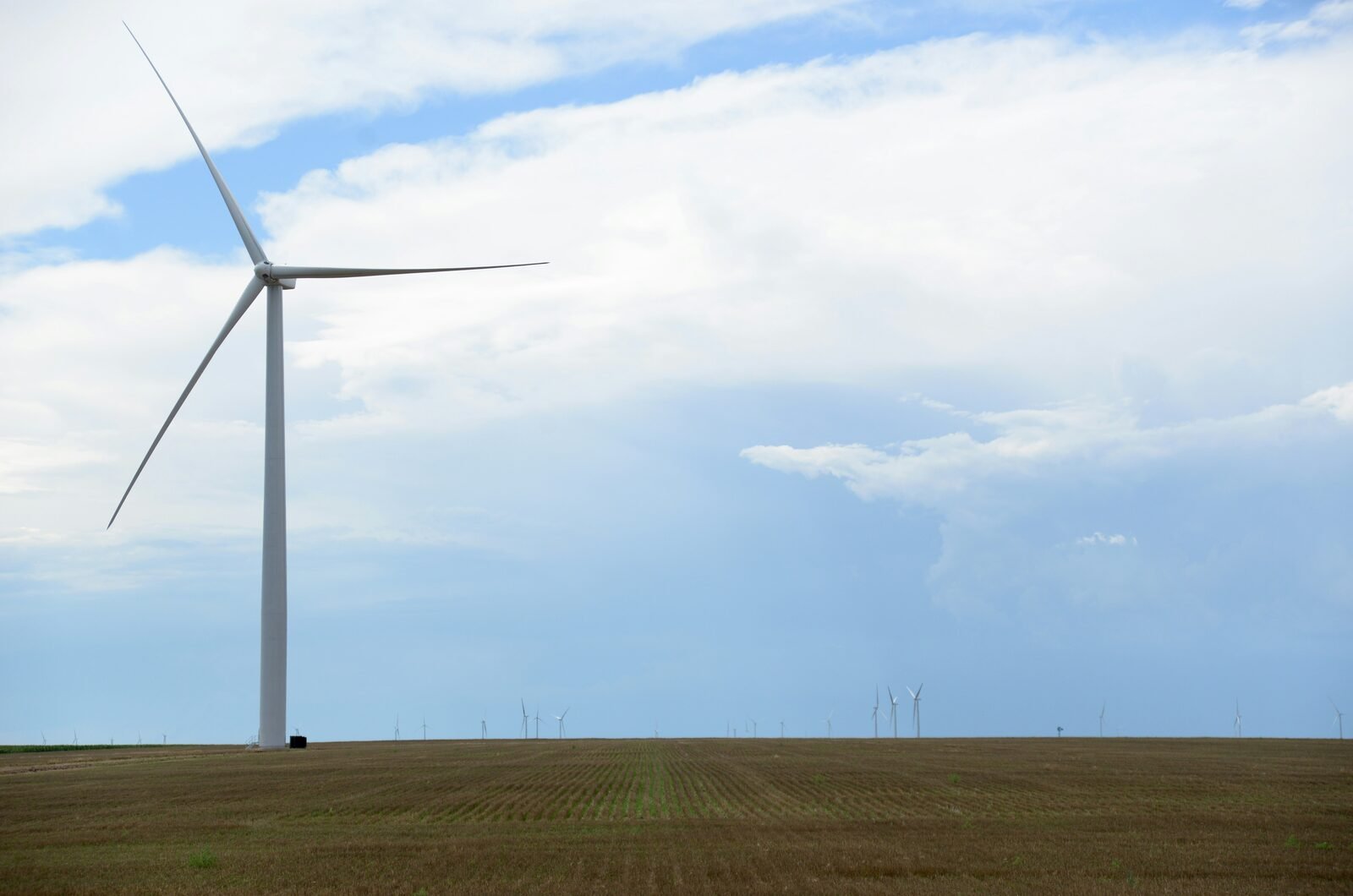 Wind turbine standing over open Great Plains farmland beneath a wide sky.